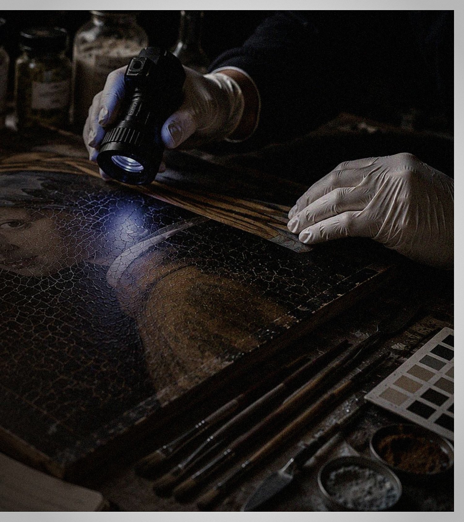 A gloved hand examines a cracked Old Master canvas under ultraviolet light.